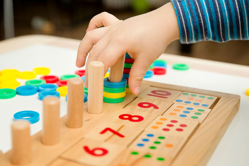 Mano de un niño acomodando aros de colores en tablero con números y puntos.