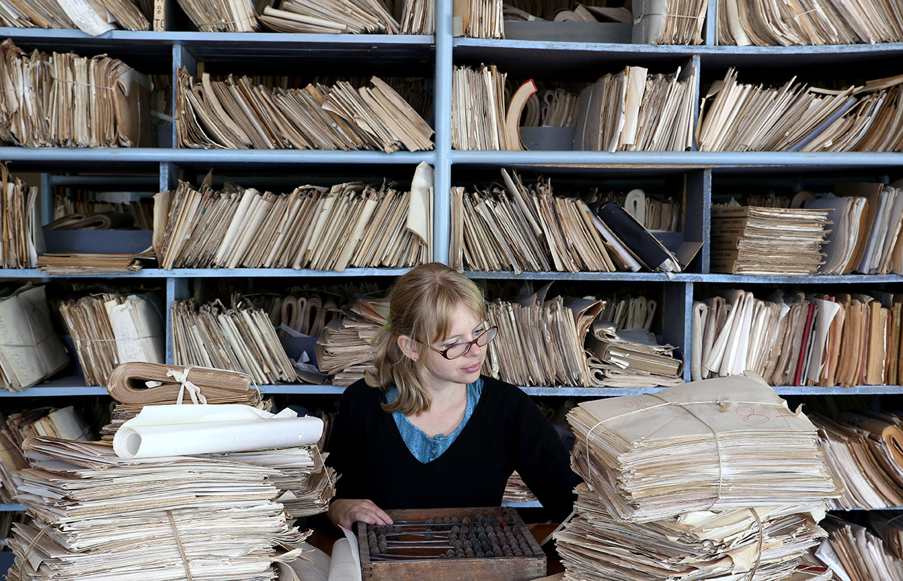 Mujer clasificando y archivando documentos antiguos en una estantería